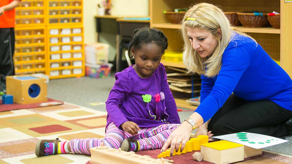 Teacher showing little girl the Montessori curriculum.